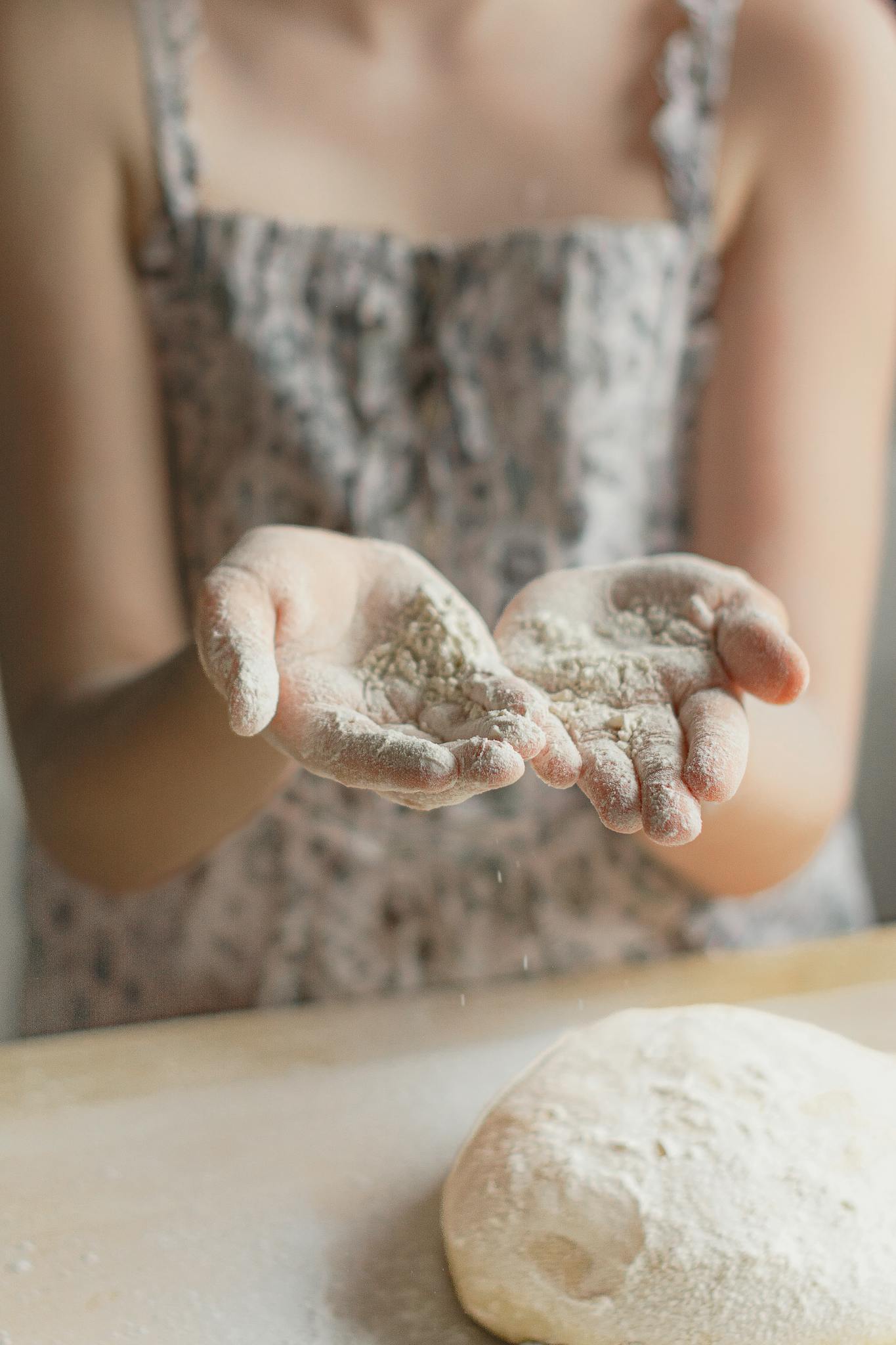 Close-up of a person dusting flour over dough on a wooden surface, creating a rustic kitchen vibe.