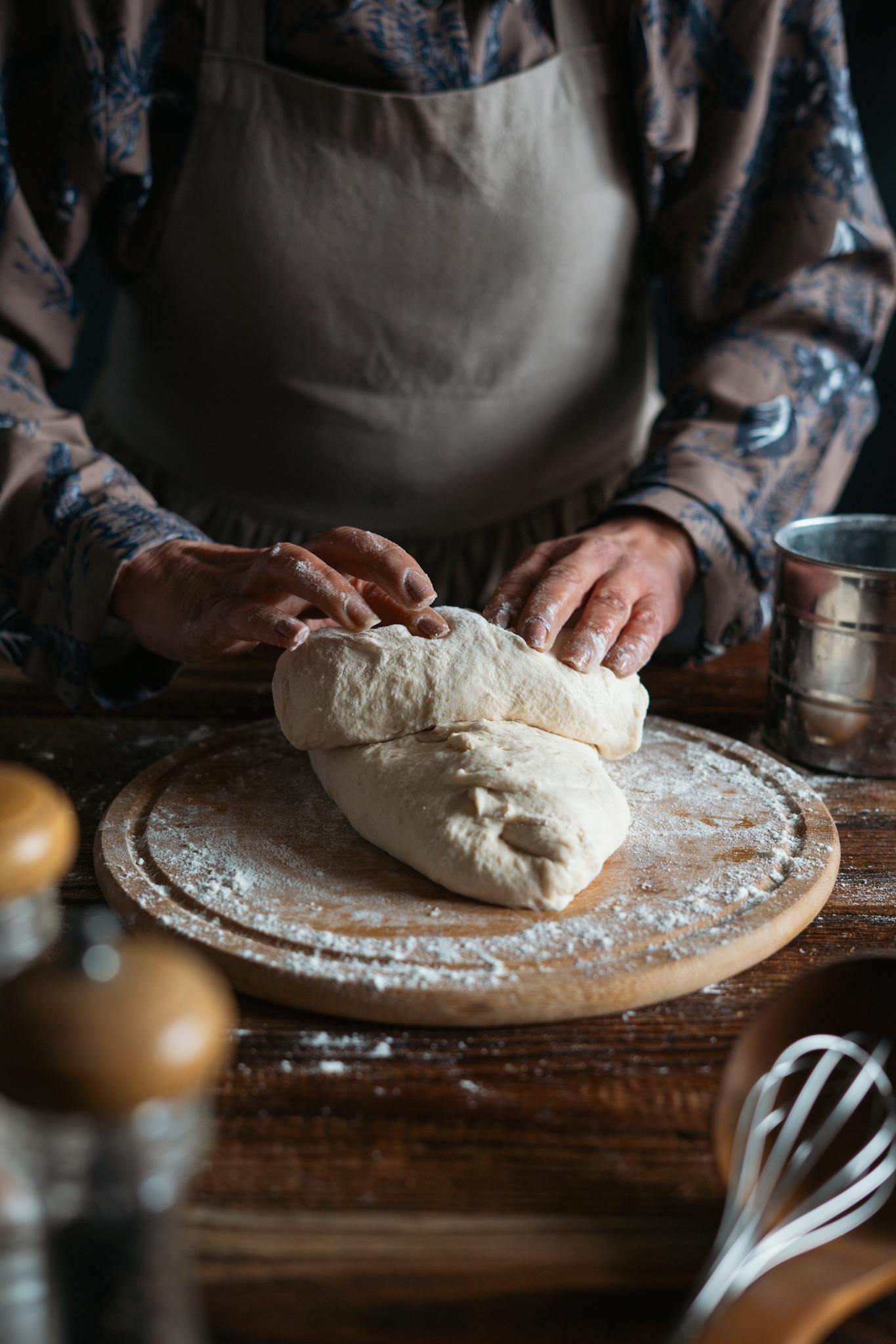 Close-up of a person kneading bread dough on a wooden board in a cozy kitchen setting.