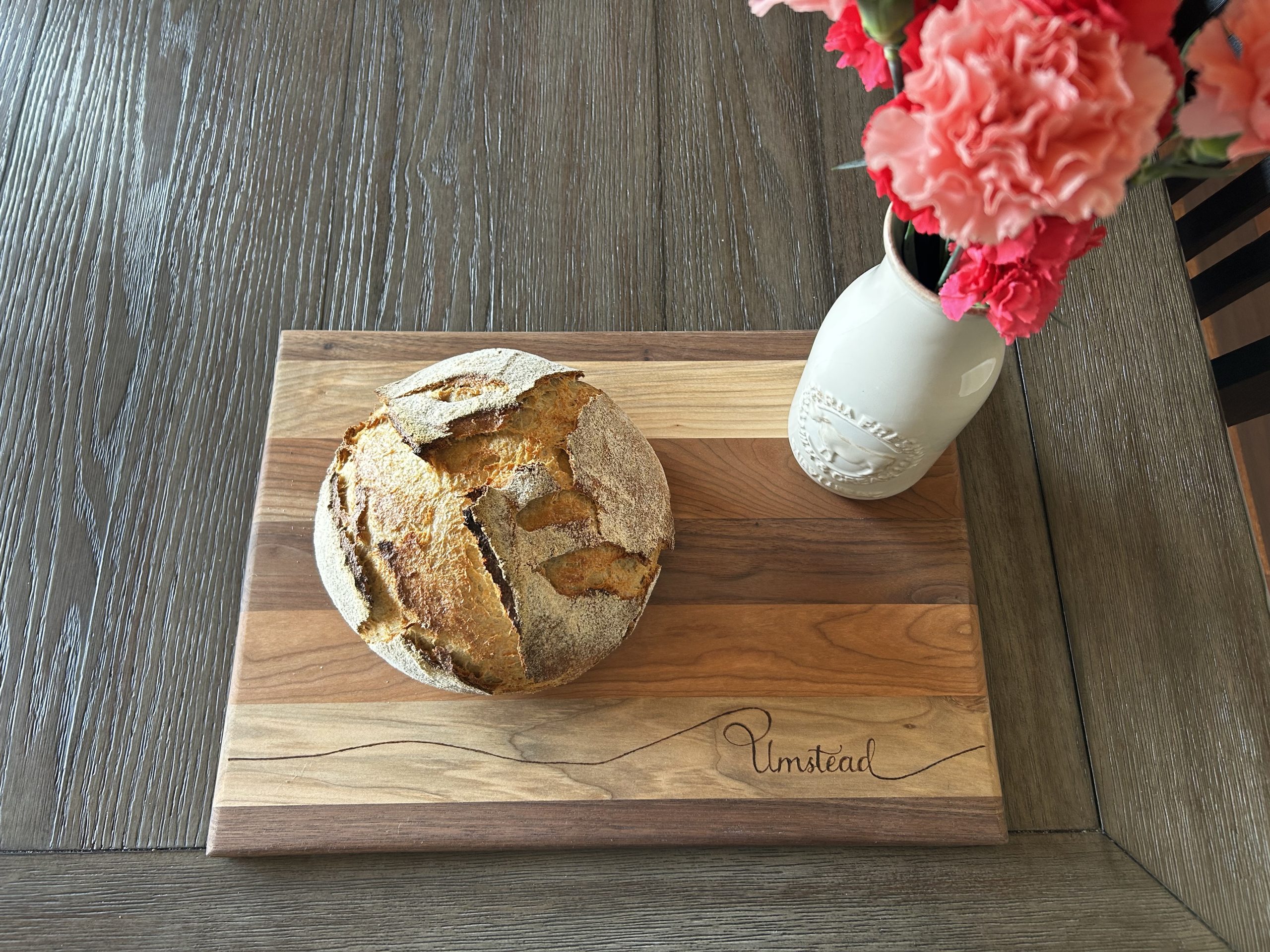 Sourdough boule and vase of pink flowers sitting on a wooden cutting board
