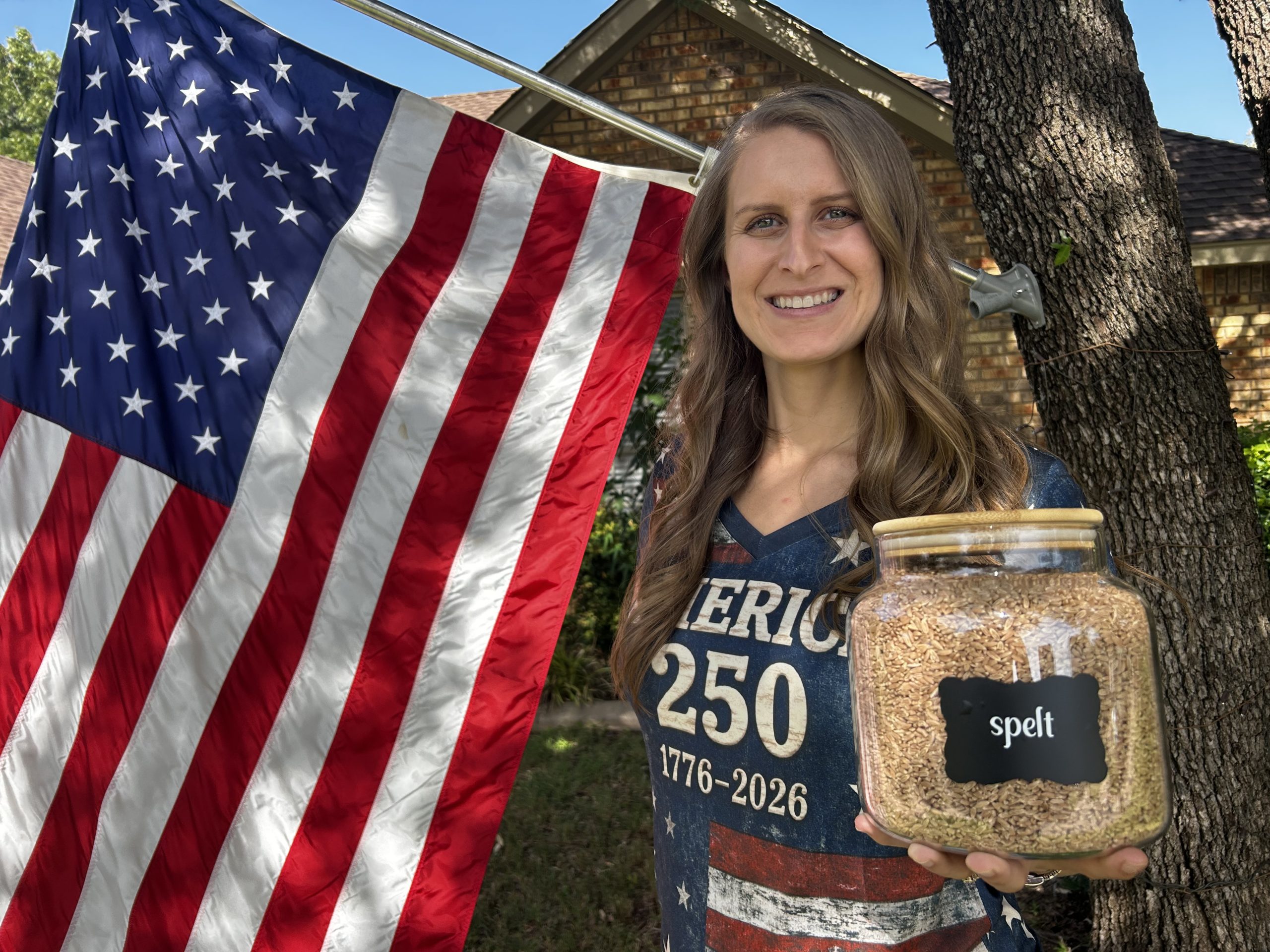 Lisa, The Fresh-Milled Wife, stands in front of American flag with a jar of spelt grain